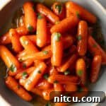 Top down bowl of glazed honey baby carrots sprinkled with chopped parsley.