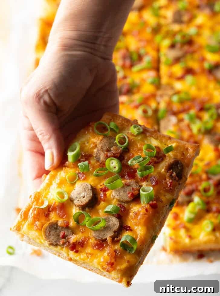 Daybreak Pizza 13 A rectangular baking sheet tray showcasing a freshly baked breakfast pizza, lavishly topped with melted cheese, savory sausage, and fresh green onions. The pizza has been expertly cut into 8 rectangular portions, with a hand reaching in to pull one inviting slice away, ready to be enjoyed.
