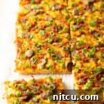 Rectangle baking sheet tray with breakfast pizza, loaded with cheese, sausage, and green onions. The pizza has been cut into 8 rectangles, with one piece pulled away.