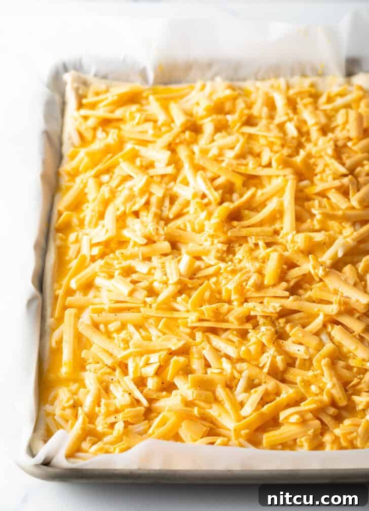 Daybreak Pizza 6 Another angle of an unbaked rectangular pizza, this time featuring a bountiful topping of shredded cheddar cheese, promising a rich, savory flavor.