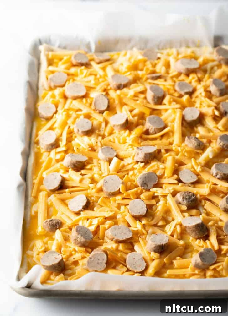 Daybreak Pizza 8 An unbaked rectangular pizza base layered with shredded mozzarella cheese and evenly distributed slices of breakfast sausage, poised for baking.