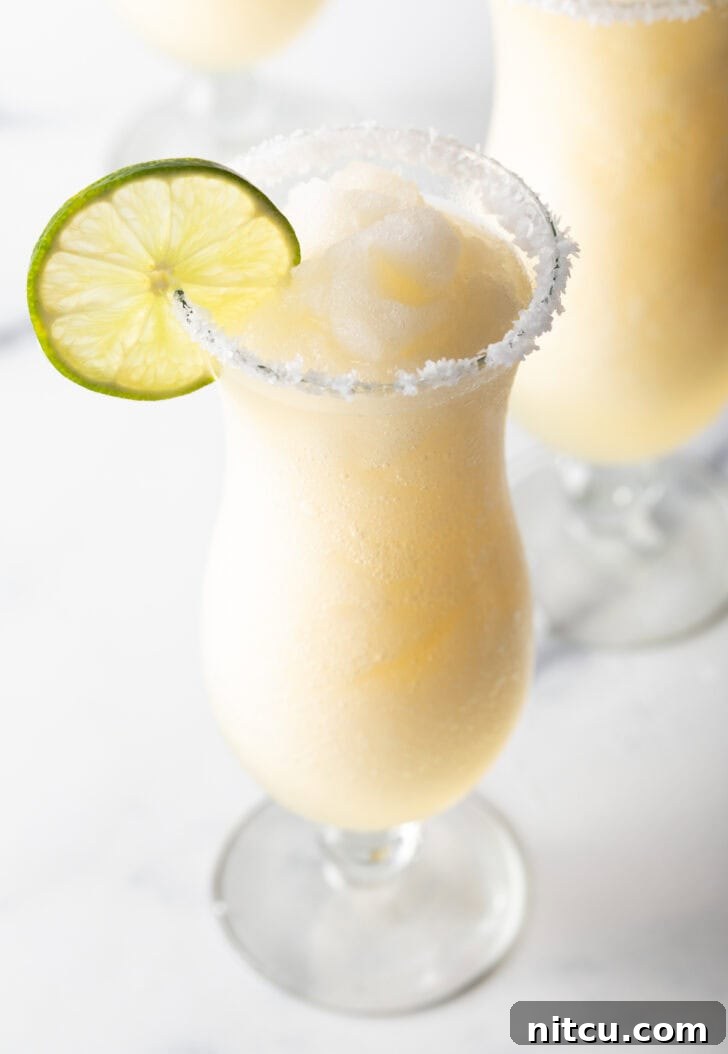 The Ultimate Frozen Margarita 2 Frozen margarita in a hurricane glass, garnished with a slice of lime and salt around the rim.