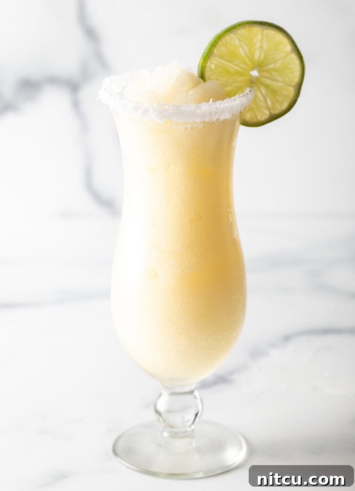 The Ultimate Frozen Margarita 12 Frozen margarita in a hurricane glass, garnished with a slice of lime and salt around the rim.
