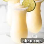 3 frozen margaritas in hurricane glasses, each garnished with a slice of lime and salt around the rim.