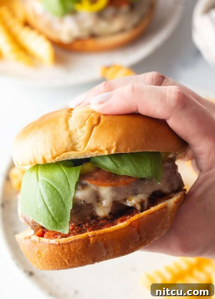 A hand enthusiastically holding up a perfectly crafted Italian pizza cheeseburger, showcasing its layers of deliciousness.