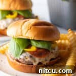 A tantalizing pizza burger on a white and black speckled plate, with a generous pile of crinkle cut french fries.