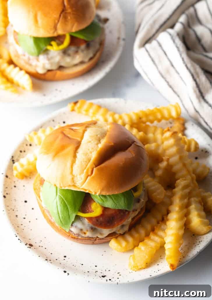 A fully assembled pizza burger, garnished with toppings, presented on a plate alongside golden french fries.