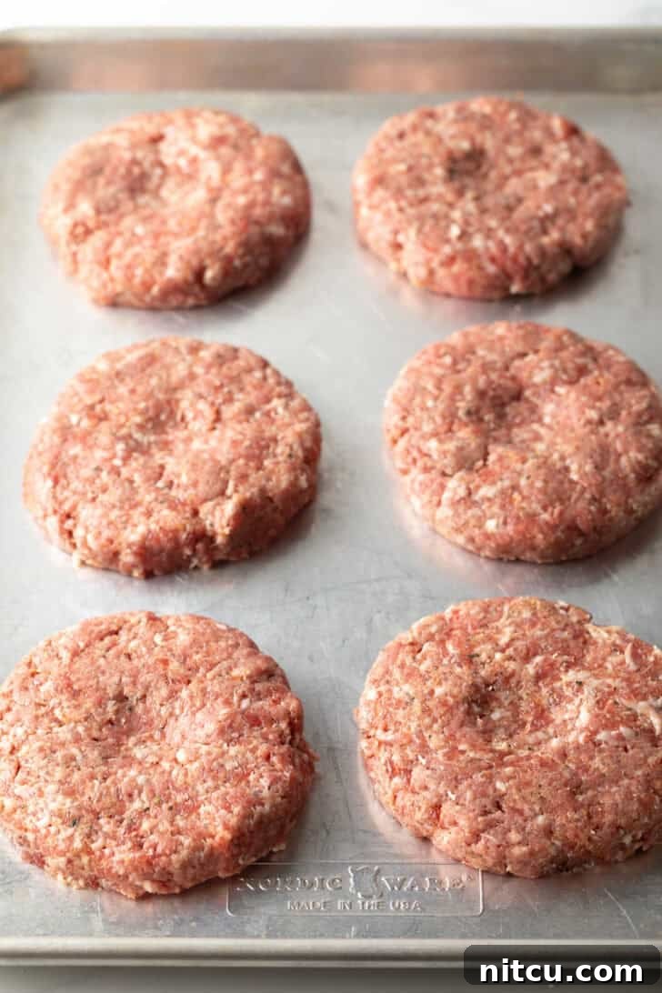 Six raw, perfectly shaped hamburger patties arranged neatly on a baking sheet, ready for cooking.