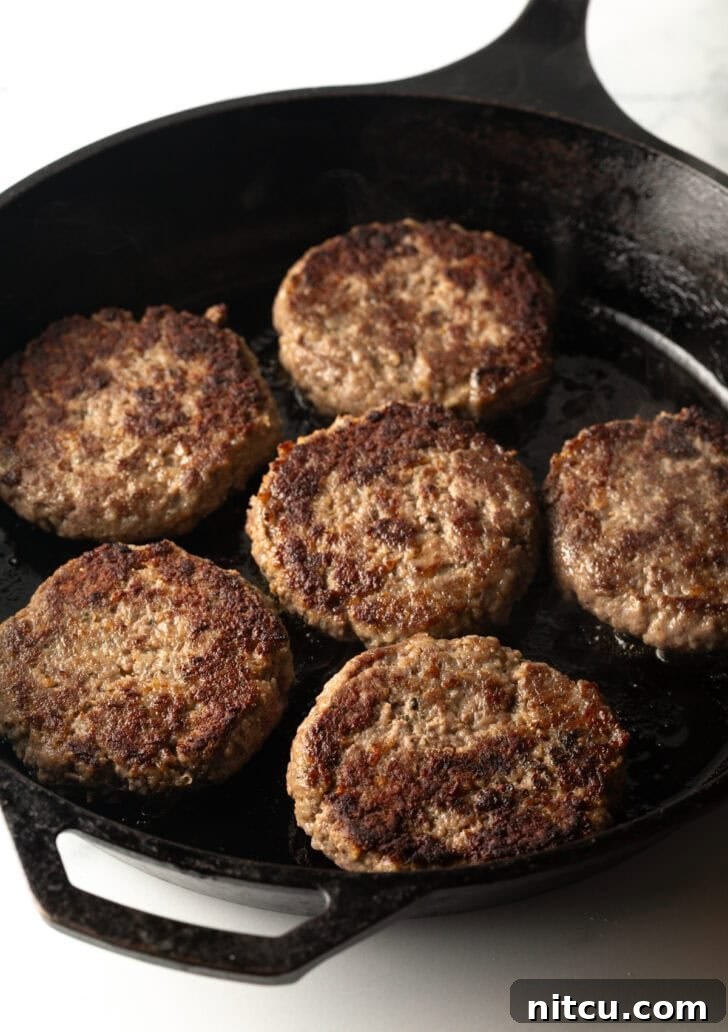 A sizzling scene of six robust hamburgers cooking evenly in a well-seasoned cast iron skillet, developing a perfect sear.