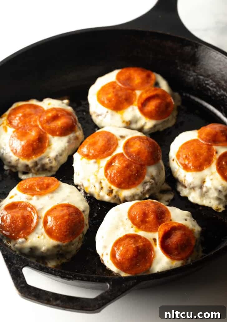 The same six burger patties, now glistening in the cast iron skillet, with perfectly melted mozzarella cheese and slightly crisped pepperoni slices.