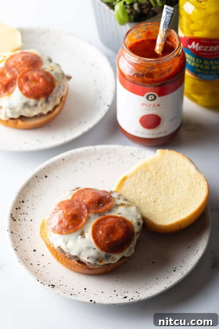 An open-faced burger on a white and black speckled plate, showcasing the bottom bun layered with sauce and a stacked burger patty crowned with melted mozzarella and pepperoni slices.