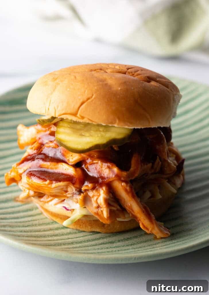 Crockpot BBQ chicken sandwich on a hamburger bun, loaded with coleslaw and pickles.