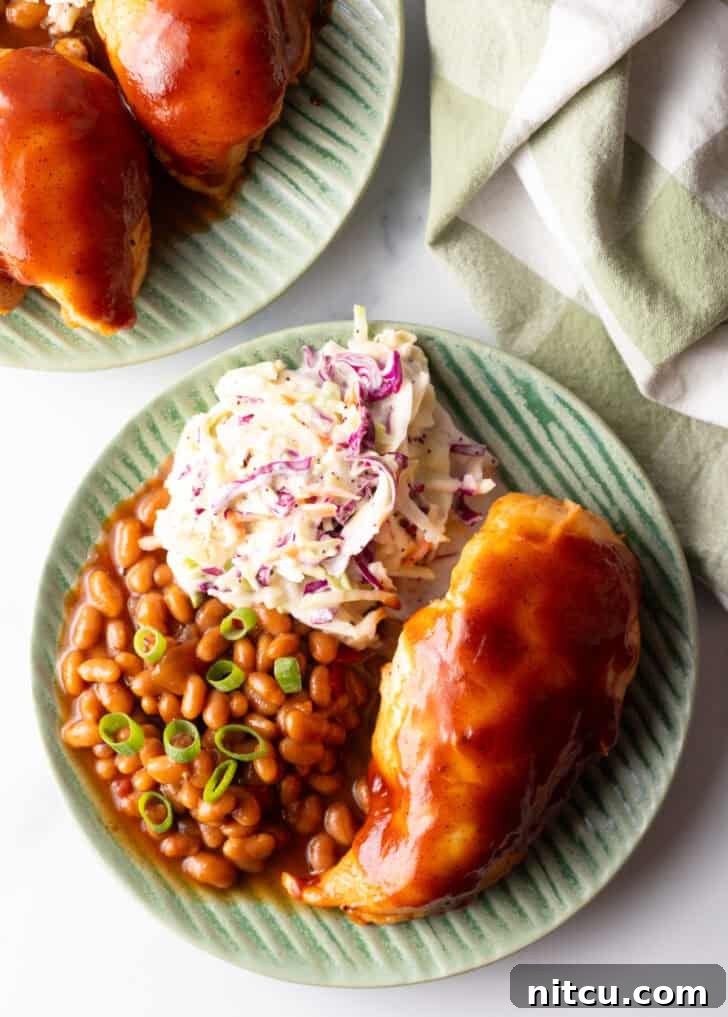 Top down view green plate with BBQ chicken, coleslaw, and baked beans.