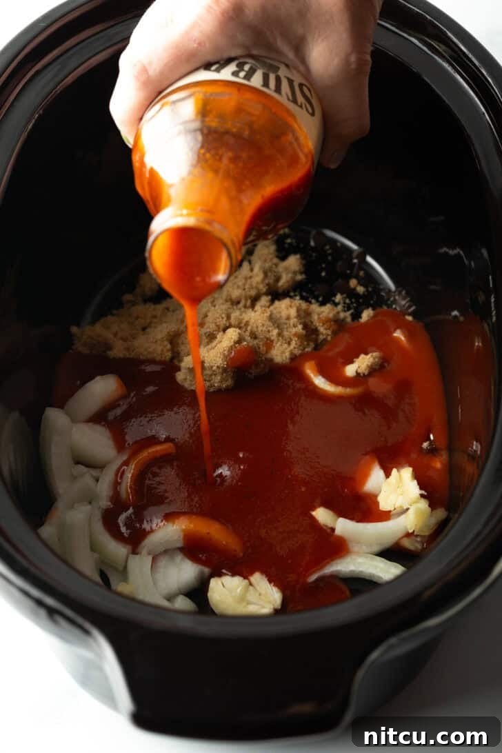 Pouring barbecue sauce from a bottle into a slow cooker with brown sugar and onion slices.