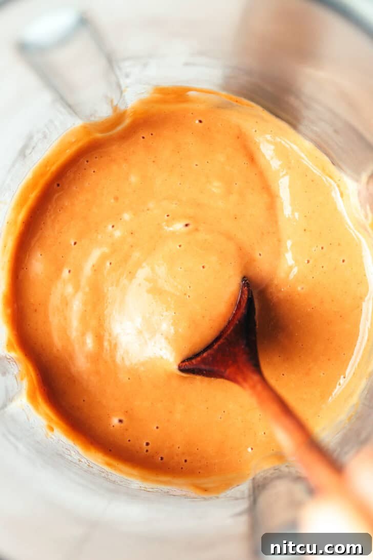 Sizzling Chicken Satay Skewers 11 A wooden spoon actively stirring the creamy peanut sauce inside a blender jar, ensuring a smooth and perfectly combined consistency.