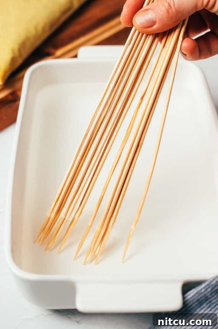 Sizzling Chicken Satay Skewers 7 A handful of wooden skewers submerged in water within a white rectangular baking dish, demonstrating the essential soaking step.