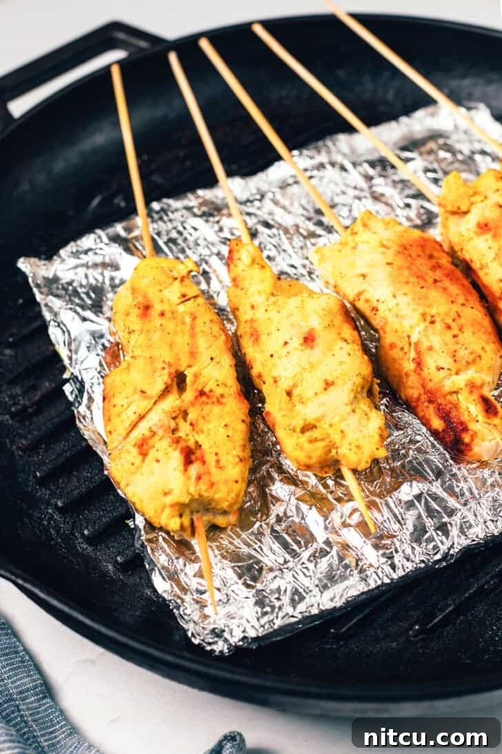 Sizzling Chicken Satay Skewers 9 Four beautifully grilled chicken skewers resting on a baking sheet lined with foil, displaying their golden-brown char marks.