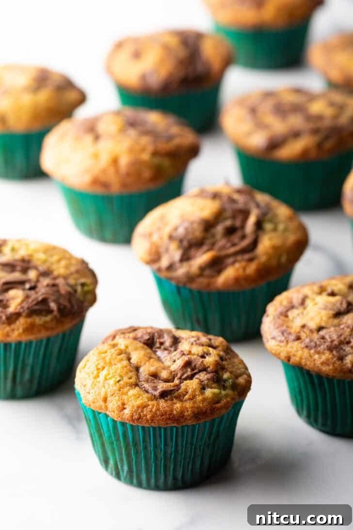 Decadent Zucchini Nutella Muffins 2 A dozen freshly baked chocolate zucchini muffins with elegant Nutella swirls, nestled in vibrant green cupcake wrappers, ready to be enjoyed.