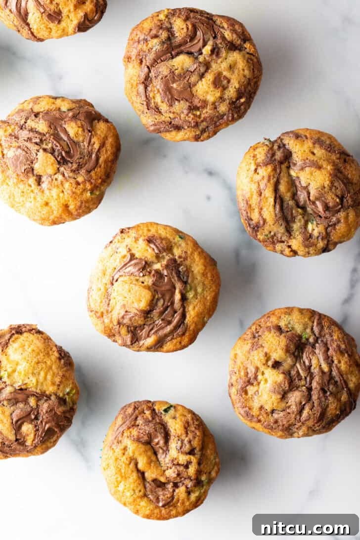 Decadent Zucchini Nutella Muffins 5 An overhead view of a dozen freshly baked chocolate zucchini muffins, beautifully swirled with chocolate, cooling in a baking tin.