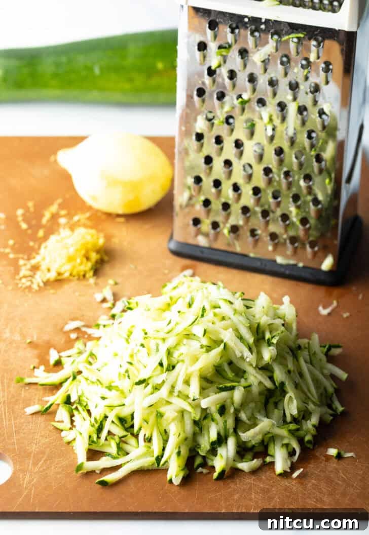 Decadent Zucchini Nutella Muffins 6 A box grater, a whole fresh lemon, and a generous pile of shredded zucchini neatly arranged on a rustic wood cutting board, showcasing the fresh ingredients.