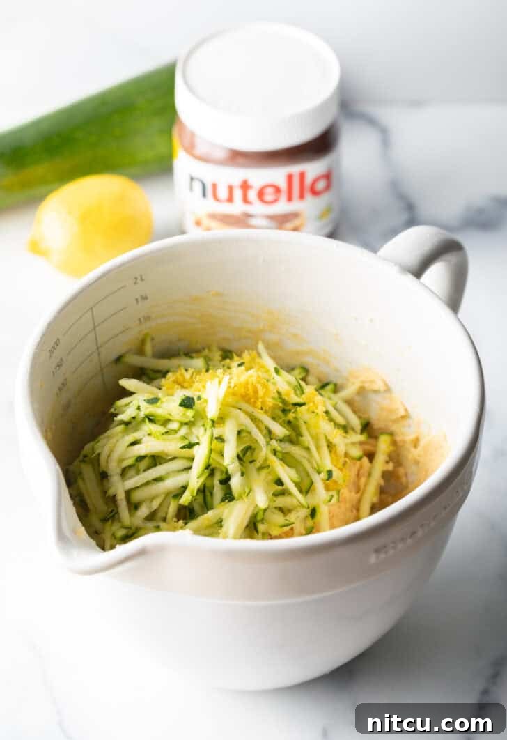 Decadent Zucchini Nutella Muffins 7 A white measuring bowl containing freshly shredded zucchini, brightened by the addition of aromatic lemon zest, ready for the muffin batter.