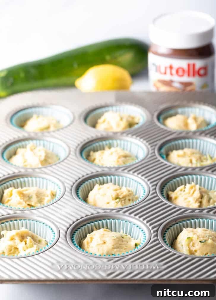 Decadent Zucchini Nutella Muffins 8 A muffin tin neatly lined with paper wrappers, each well filled with a portion of the moist zucchini muffin batter, awaiting the next step.