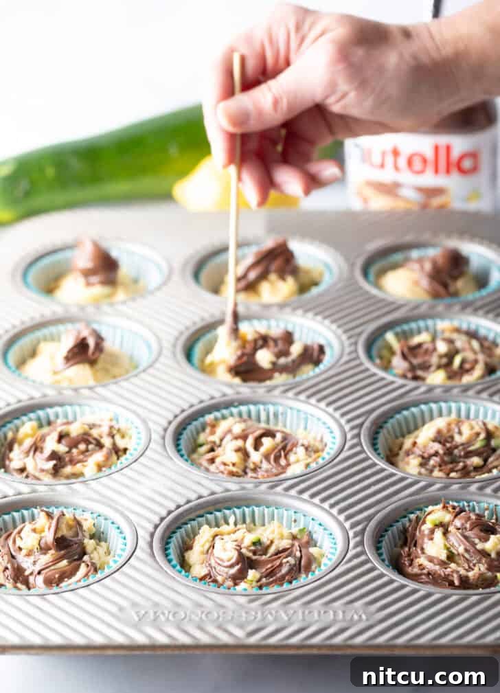 Decadent Zucchini Nutella Muffins 10 A hand skillfully using a wooden skewer to gently swirl Nutella into the unbaked zucchini muffin batter within a baking tin, creating beautiful marble patterns.