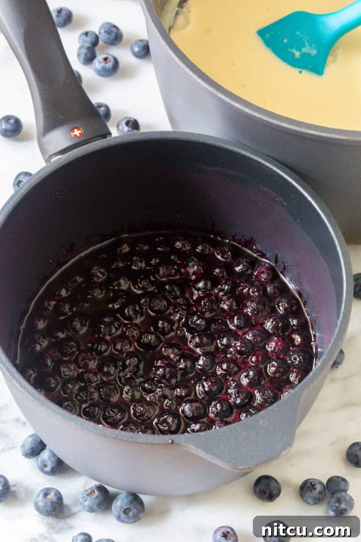 Berry Bliss Freeze 10 Cooking blueberries in a metal cooking pot on a stovetop.