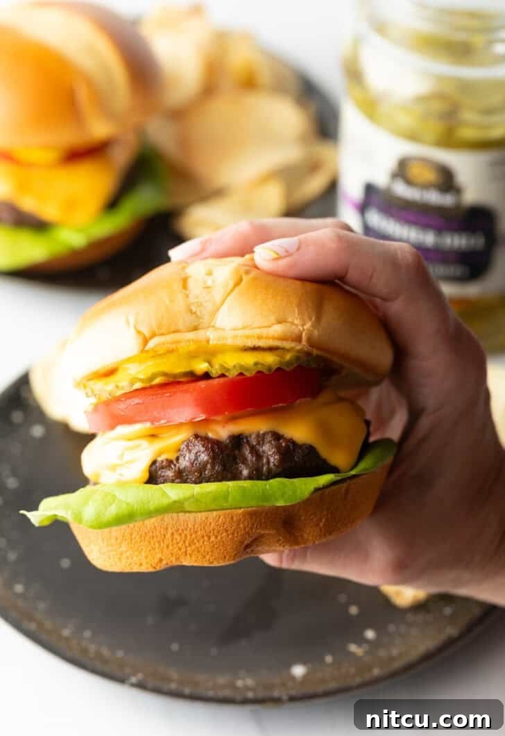 Hand holding a juicy air fryer hamburger loaded with cheese, lettuce, tomatoes and pickle slices.