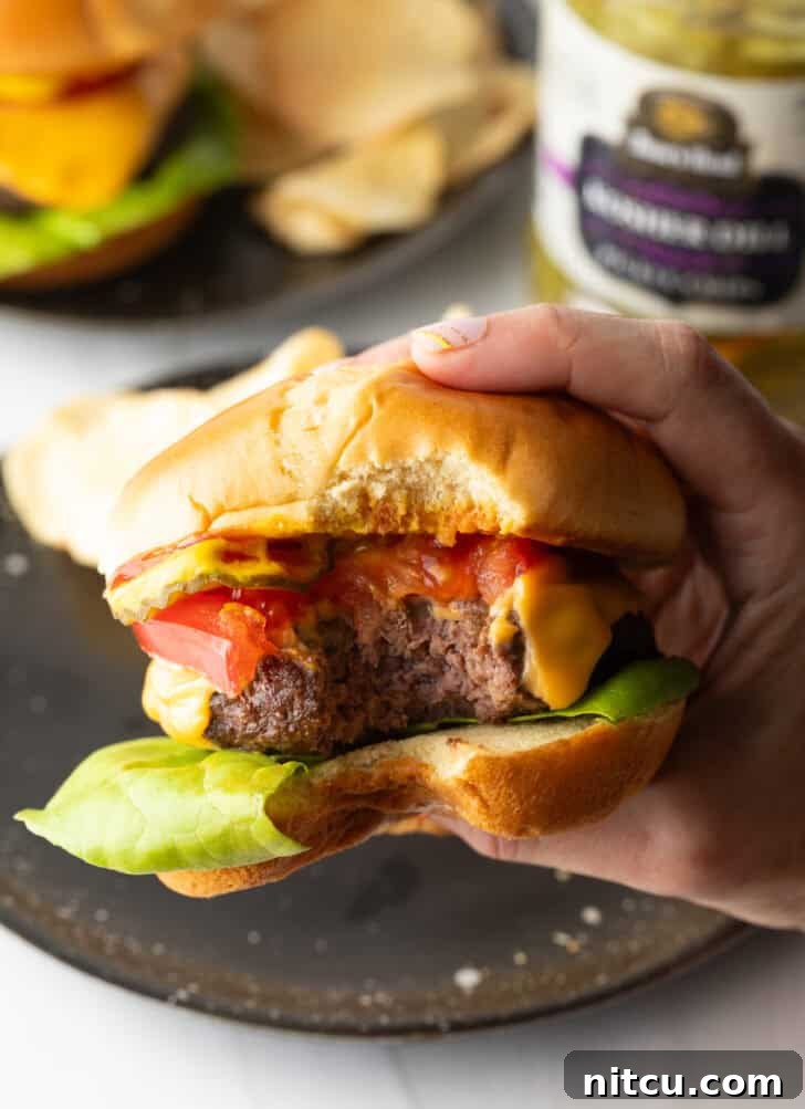 Hand holding a hamburger to camera, with bite taken out.