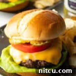 Aair fryer hamburger loaded with cheese, lettuce, tomatoes and pickle slices on a plate.