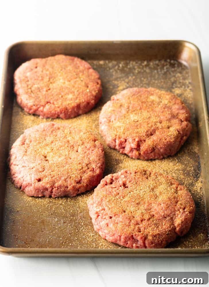 4 raw seasoned burger patties on a baking sheet.