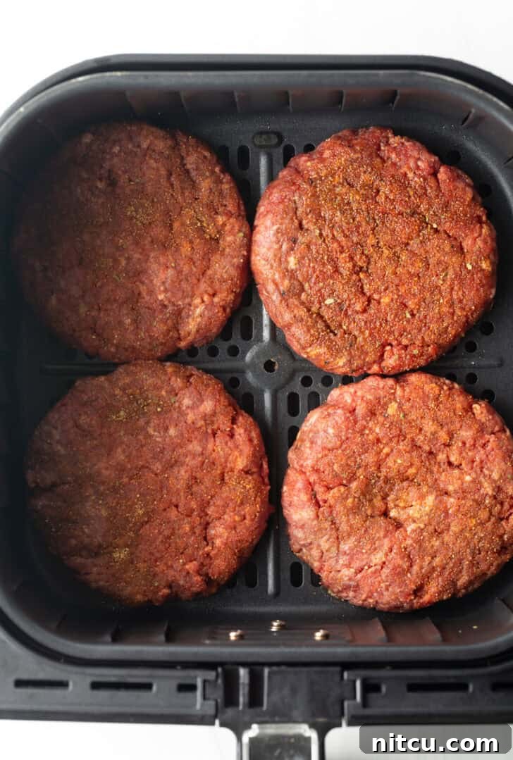 Top down view 4 hamburger patties in an air fryer basket.