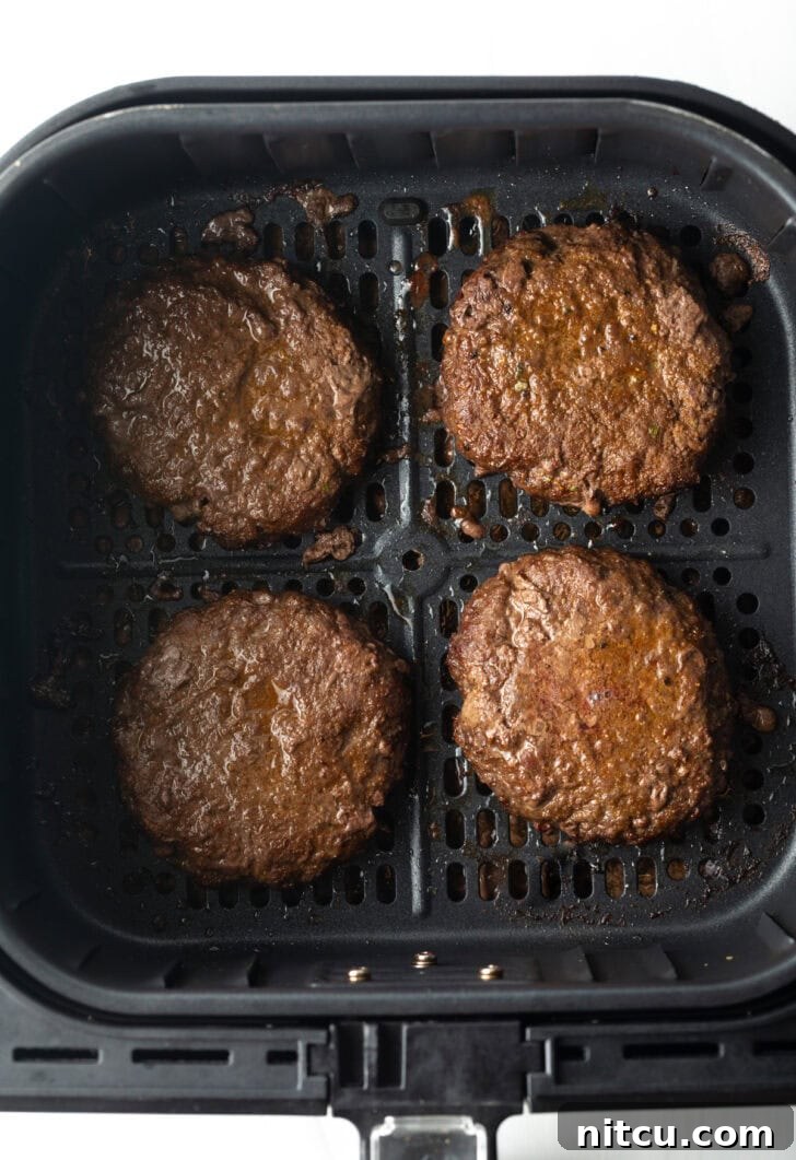 Top down view 4 burgers in an air fryer basket.