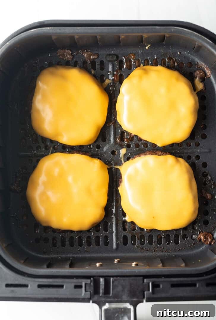 Top down view 4 cheeseburgers in an air fryer basket.