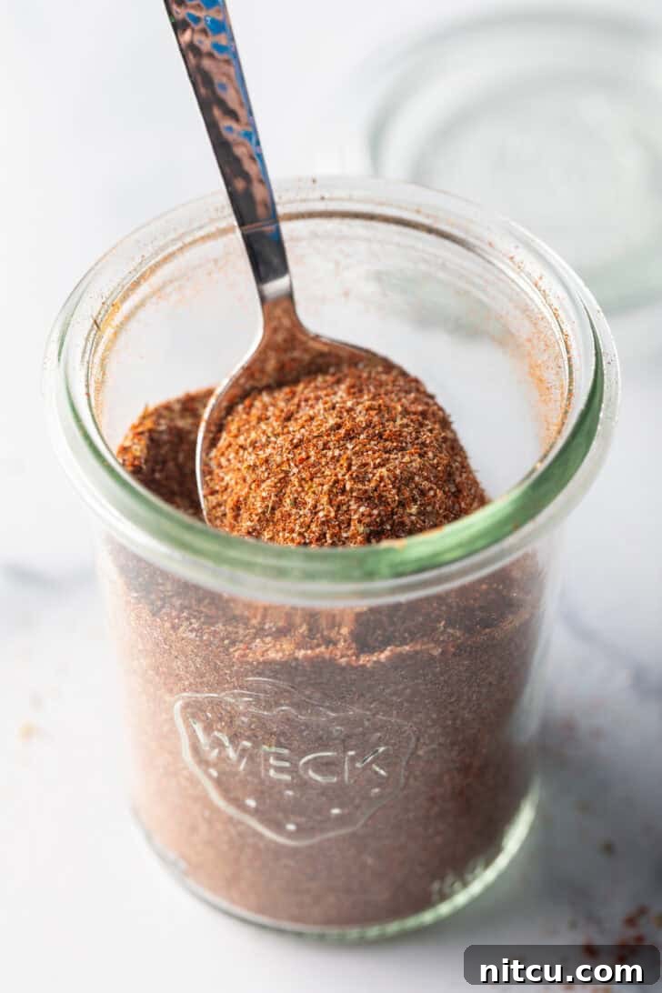 Zesty Chicken Taco Blend 9 A spoon scooping a portion of the rich, aromatic chicken taco seasoning from a small glass jar.
