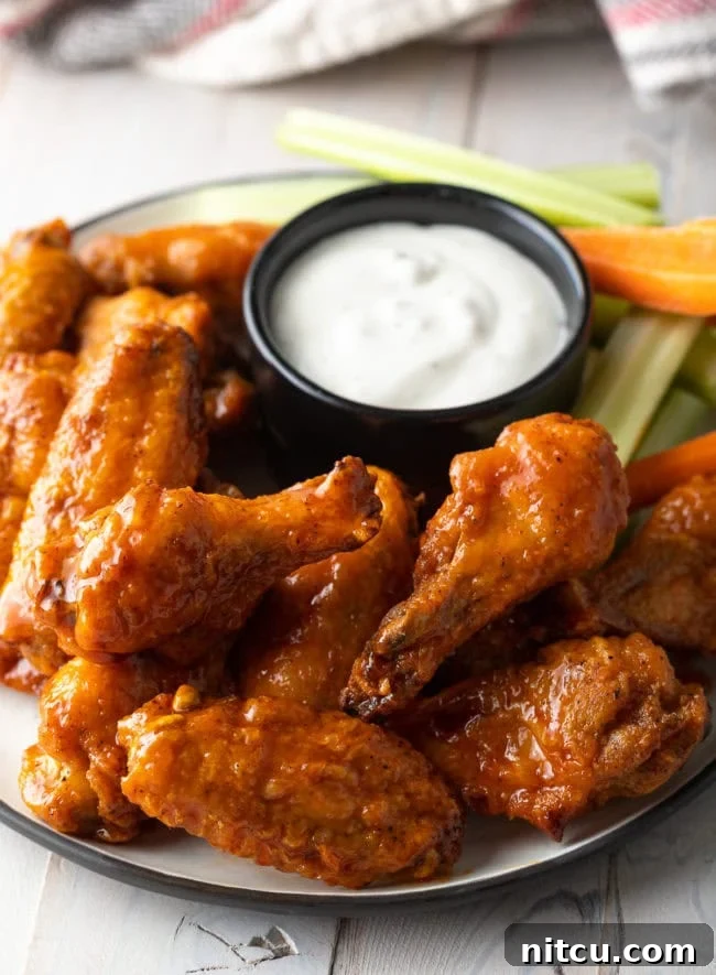 Plateful of baked buffalo chicken wings with black ramekin of ranch dressing, carrot sticks and celery sticks.