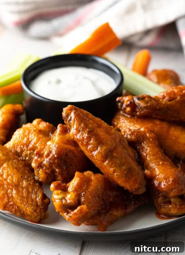 Plateful of oven baked chicken wings with black ramekin of ranch dressing, carrot sticks and celery sticks.