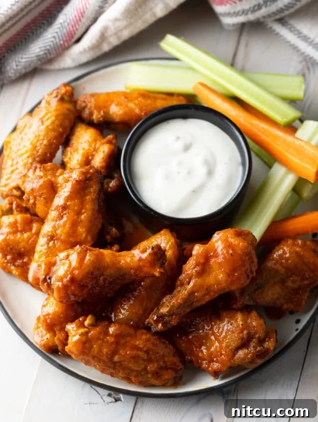 Plateful of oven baked chicken wings with black ramekin of ranch dressing, carrot sticks and celery sticks.