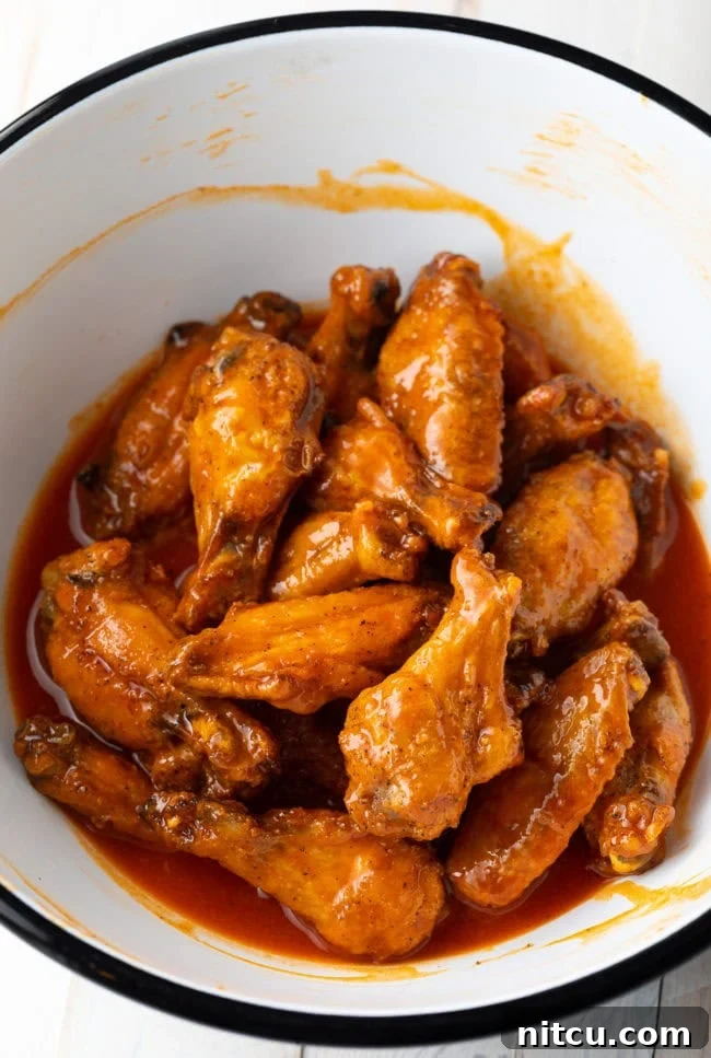 White mixing bowl tossing chicken wings in buffalo sauce.