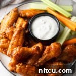 Plateful of baked buffalo chicken wings with black ramekin of ranch dressing, carrot sticks and celery sticks.