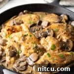 Creamy Mushroom Chicken Delight 13 Mushroom Chicken - Cast iron skillet brimming with seared chicken breast pieces and sliced mushrooms in a rich brown gravy.