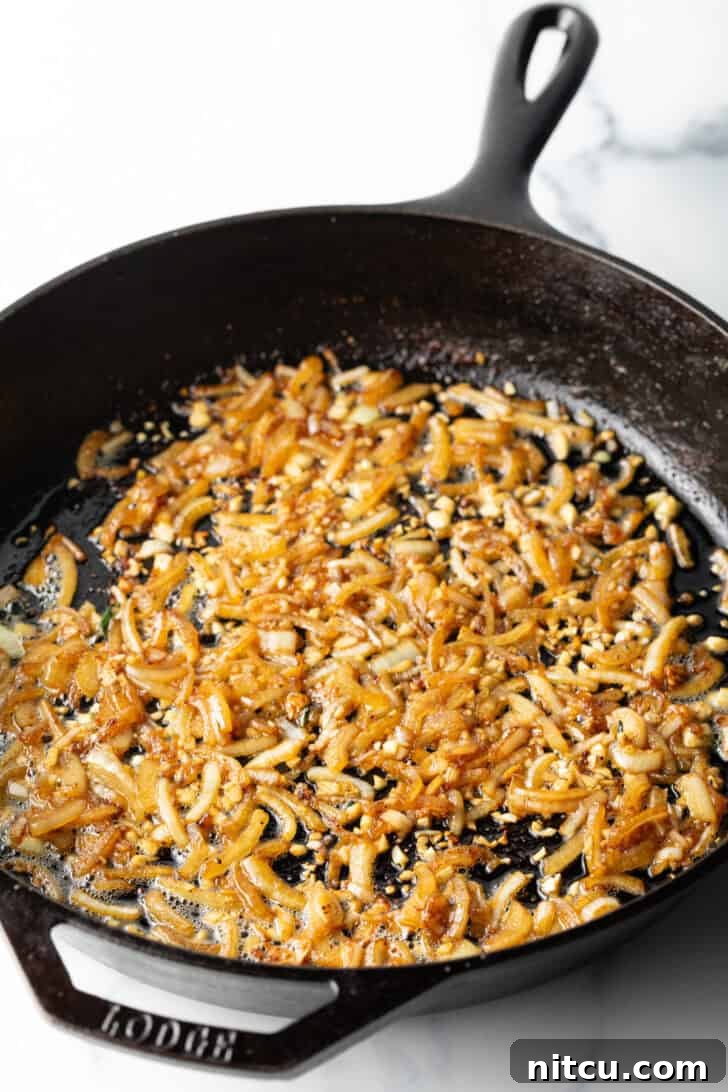 Creamy Mushroom Chicken Delight 7 Diced onions and minced garlic browning in a cast iron skillet, releasing fragrant aromas.