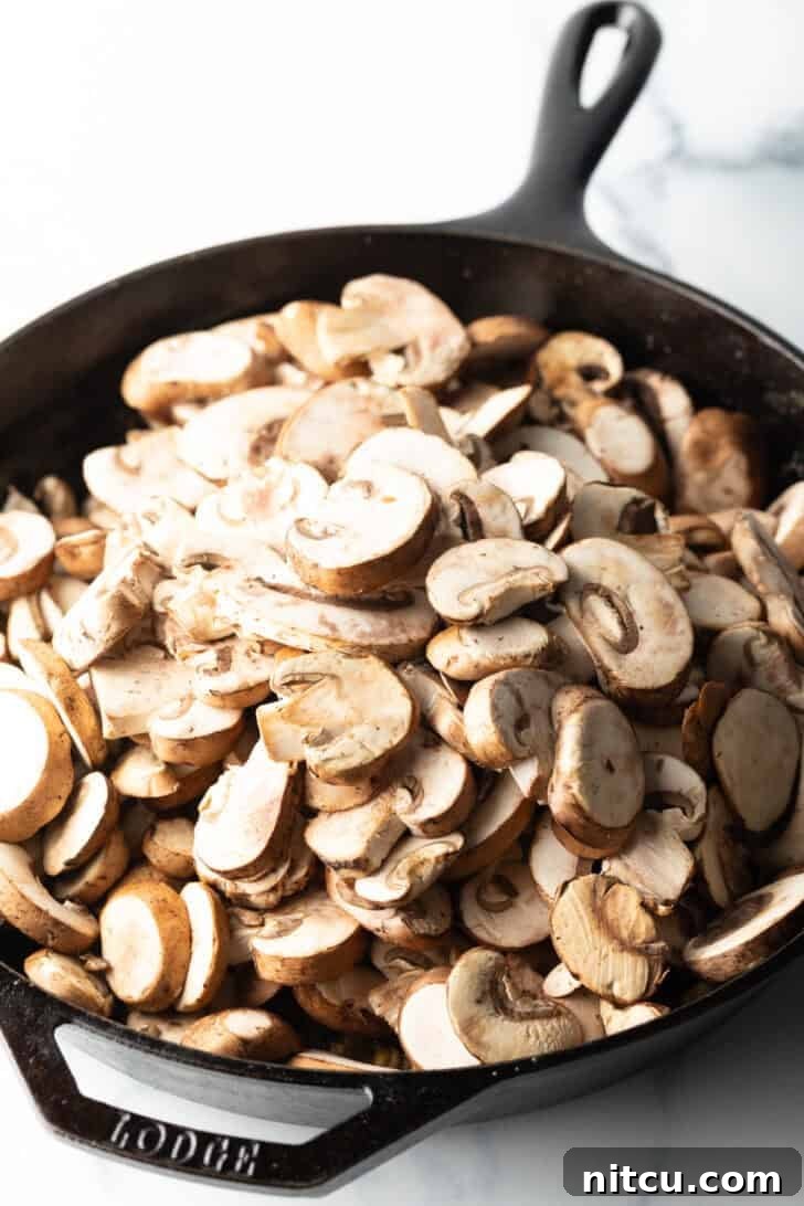 Creamy Mushroom Chicken Delight 8 Freshly sliced button mushrooms being added to a cast iron skillet.