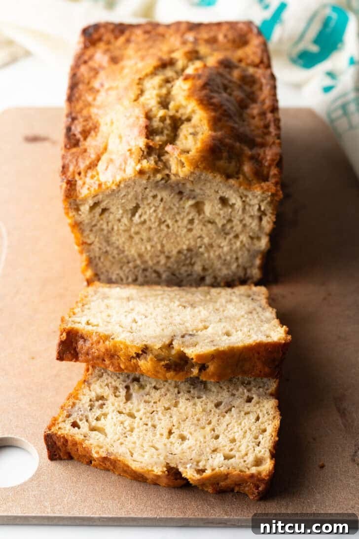 Effortless Banana Bread 2 A freshly baked loaf of golden-brown banana bread on a wooden cutting board, with two inviting slices already cut and visible.
