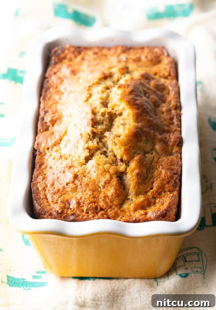 Effortless Banana Bread 11 A beautifully baked 4-ingredient banana bread loaf, golden brown and still warm, resting in a white and yellow patterned loaf pan.