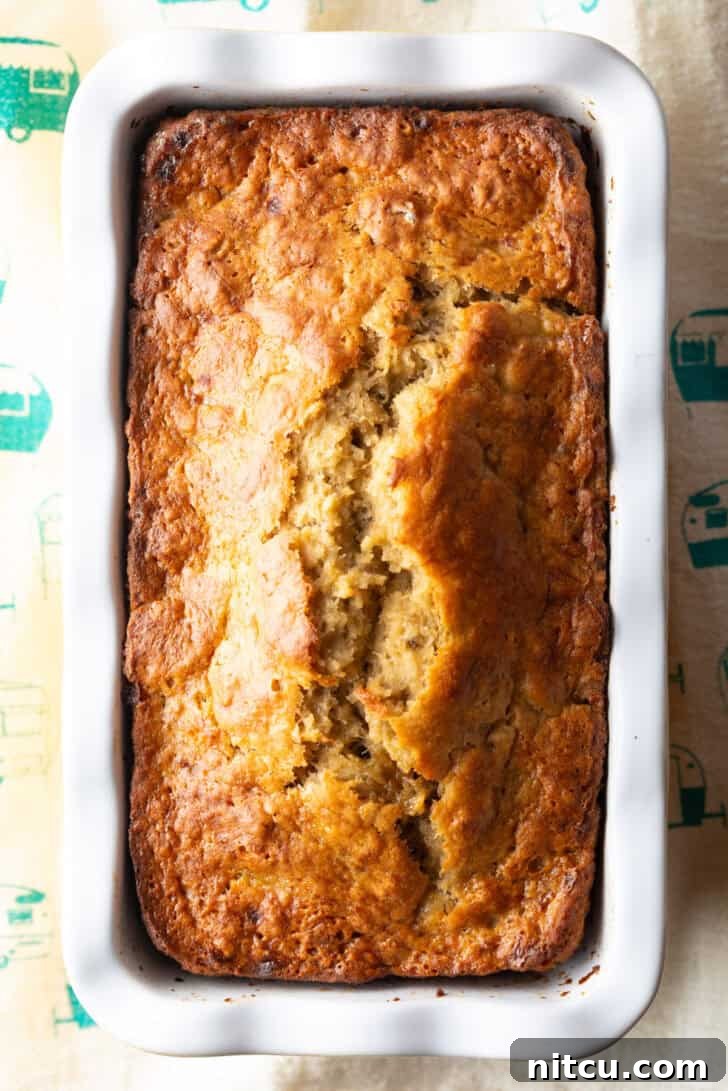 Effortless Banana Bread 12 Top-down view of a perfectly baked 4-ingredient banana bread loaf, golden brown and enticing, still nestled in its white and yellow loaf pan.