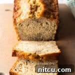 Loaf of banana bread on a cutting board, with two slices showing to camera.