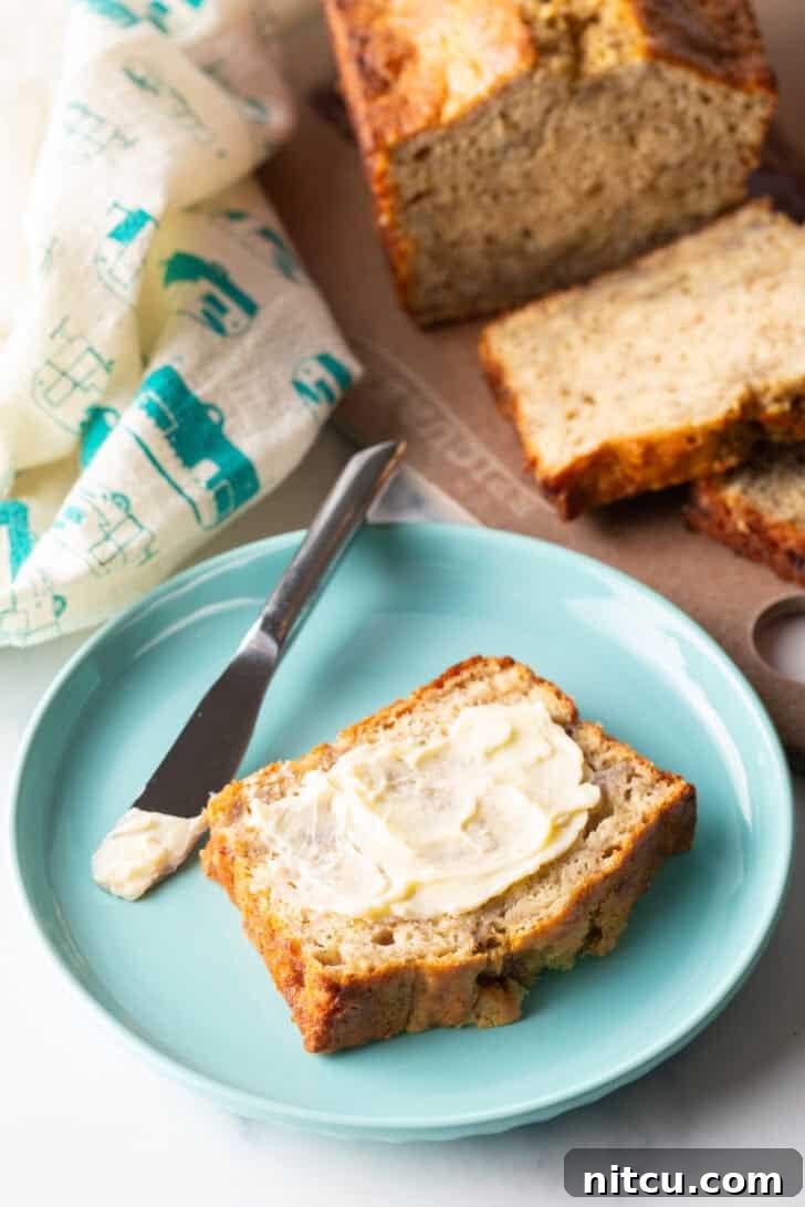 Effortless Banana Bread 14 A beautifully sliced piece of 4-ingredient banana bread, glistening with melted butter, presented on a vibrant blue plate alongside a knife.