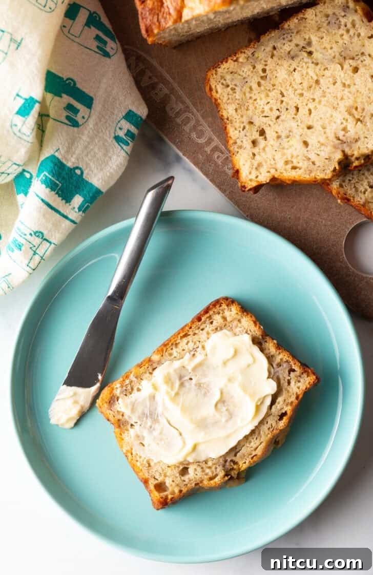 Effortless Banana Bread 4 A delicious slice of 4-ingredient banana bread, generously spread with butter, resting on a charming blue plate beside a knife.